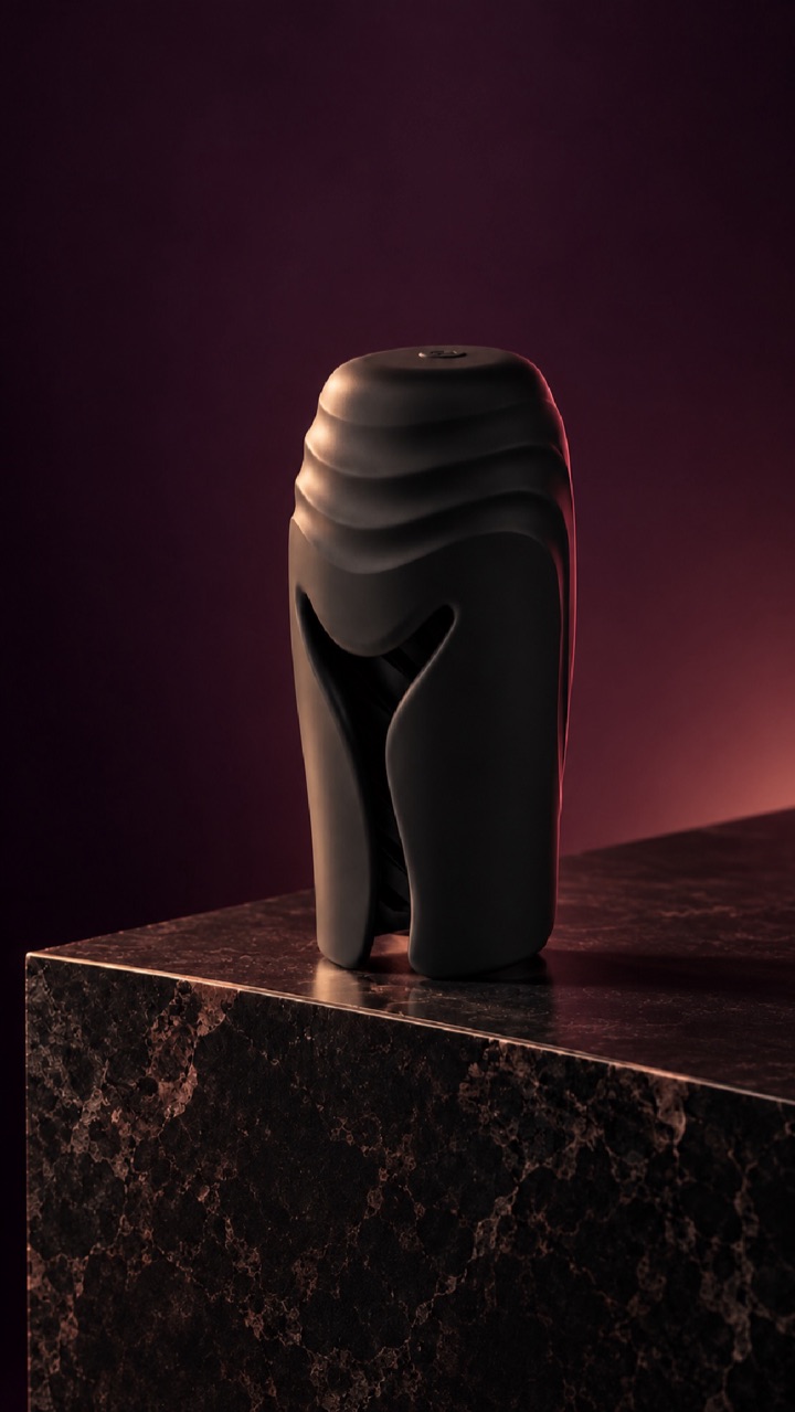 A sculptural, unbranded device in dark silicone on a marble plinth, lit in deep red.